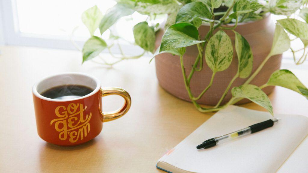 black retractable pen on opened book beside red and white go get'em-printed coffee cup